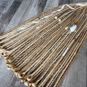 May include: A set of brown and blonde synthetic dreadlocks with beads, lace, and feathers. The dreadlocks are arranged in a fan shape on a wooden surface.