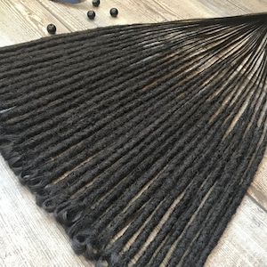 May include: A set of black synthetic dreadlocks, arranged in a fan shape on a wooden surface.