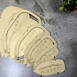 Op de afbeelding: Een set van acht houten sjablonen in verschillende maten, variërend van 17 cm tot 28 cm. Elke sjabloon heeft een gebogen vorm met een decoratief ontwerp en afmetingen in inches en centimeters.