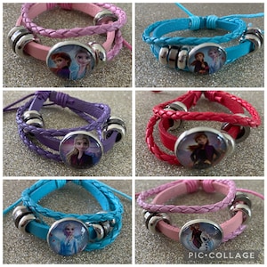 Könnte beinhalten: Sechs verschiedene geflochtene Lederarmbänder in verschiedenen Farben, darunter Pink, Blau, Lila und Rot. Jedes Armband hat einen runden, silberfarbenen Anhänger mit einem Bild von Figuren aus dem Film Frozen.