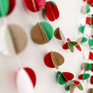 May include: A festive garland made of paper circles in red, green, brown, and white. The circles are layered and folded to create a 3D effect. The garland is strung together with white thread.