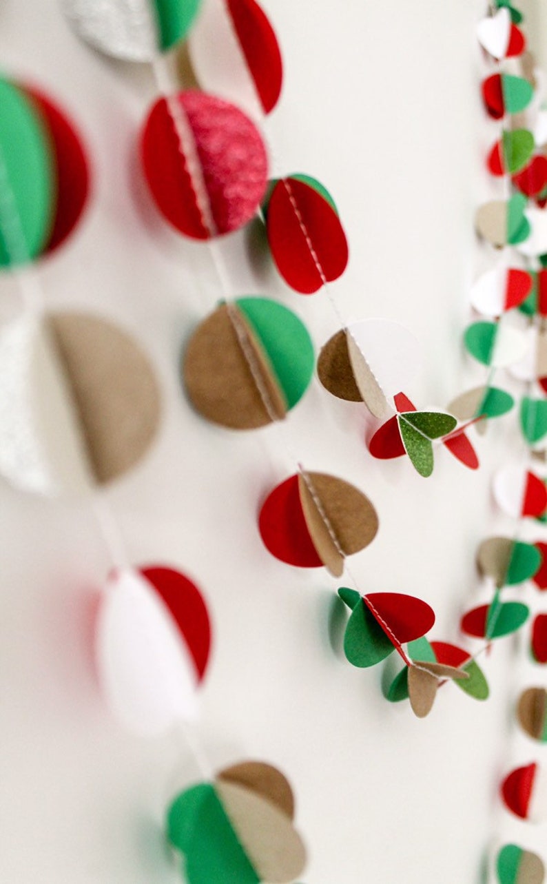 May include: A festive garland made of paper circles in red, green, brown, and white. The circles are layered and folded to create a 3D effect. The garland is strung together with white thread.