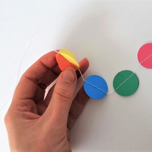 May include: A string of colorful paper circles strung together with white thread. The circles are yellow, orange, pink, blue, and green.