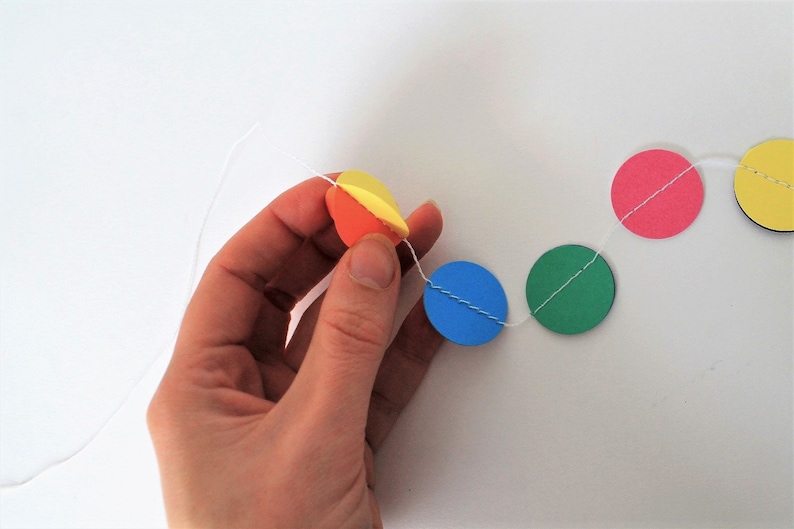 May include: A string of colorful paper circles strung together with white thread. The circles are yellow, orange, pink, blue, and green.