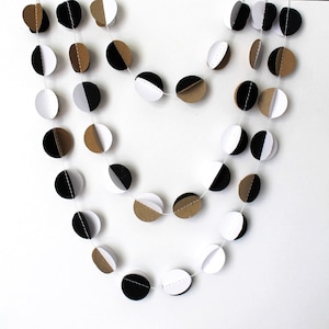 May include: A black, white, and brown paper garland with circles cut in half. The circles are strung together with white thread.