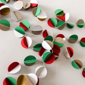 May include: A festive paper garland with red, green, white, brown, and gold circles. The circles are strung together with white thread.