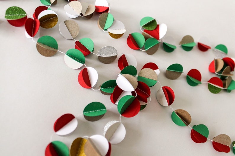 May include: A festive paper garland with red, green, white, brown, and gold circles. The circles are strung together with white thread.