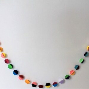 May include: A colorful paper garland with circles in various colors, including green, yellow, pink, blue, and black. Each circle is cut in half and the two halves are joined together to create a three-dimensional effect.