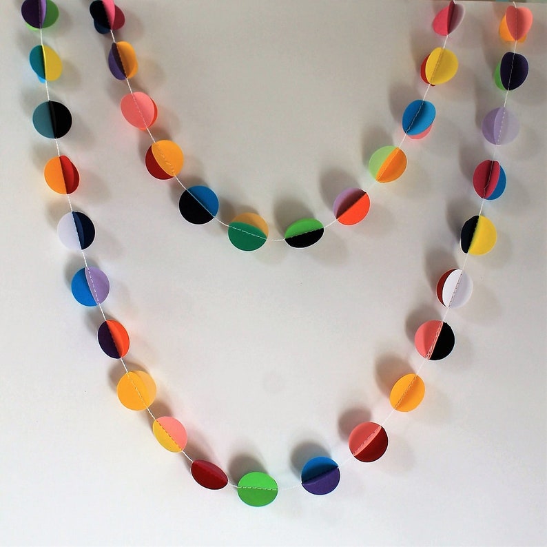 May include: A colorful paper garland with alternating circles of red, orange, yellow, green, blue, purple, and white. The circles are strung together with white thread.