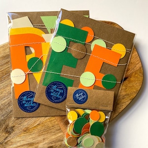 May include: A set of three brown paper cards with the letters "REF" cut out in orange, green, and brown paper. The letters are decorated with small circles of orange, green, and brown paper. The cards are packaged in clear plastic bags with a sticker that says "Always in Stitches". A small bag of assorted paper circles in orange, green, brown, and cream is also included.