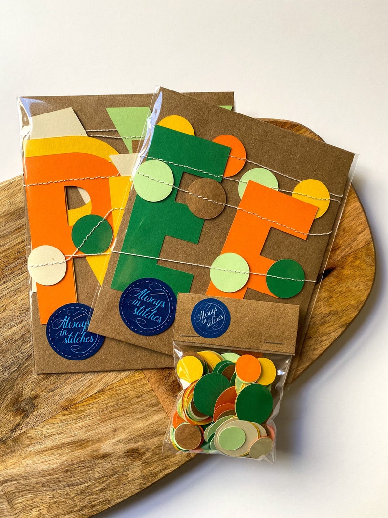 May include: A set of three brown paper cards with the letters "REF" cut out in orange, green, and brown paper. The letters are decorated with small circles of orange, green, and brown paper. The cards are packaged in clear plastic bags with a sticker that says "Always in Stitches". A small bag of assorted paper circles in orange, green, brown, and cream is also included.