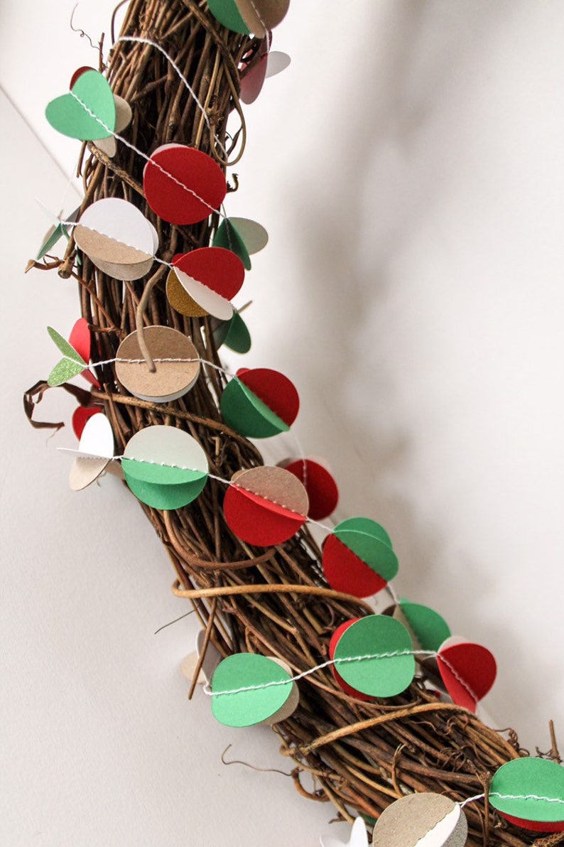 May include: A brown twig wreath decorated with a garland of paper circles in red, green, white, and brown. The garland is strung with white thread.