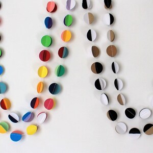 May include: Two paper garlands with colorful circles. The first garland has circles with alternating colors of red, yellow, green, blue, purple, and black. The second garland has circles with alternating colors of brown, white, and black.