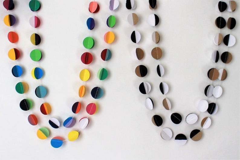 May include: Two paper garlands with colorful circles. The first garland has circles with alternating colors of red, yellow, green, blue, purple, and black. The second garland has circles with alternating colors of brown, white, and black.