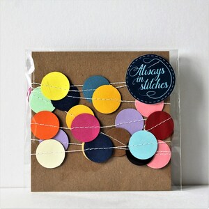 May include: A brown card with a string of colorful paper circles and the text "Always in stitches" on a blue circle.