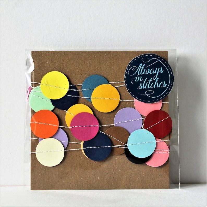 May include: A brown card with a string of colorful paper circles and the text "Always in stitches" on a blue circle.