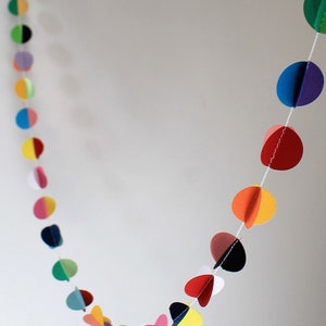 May include: A colorful paper garland with circles of different colors, including red, orange, yellow, green, blue, purple, and pink. The circles are connected by a white string.