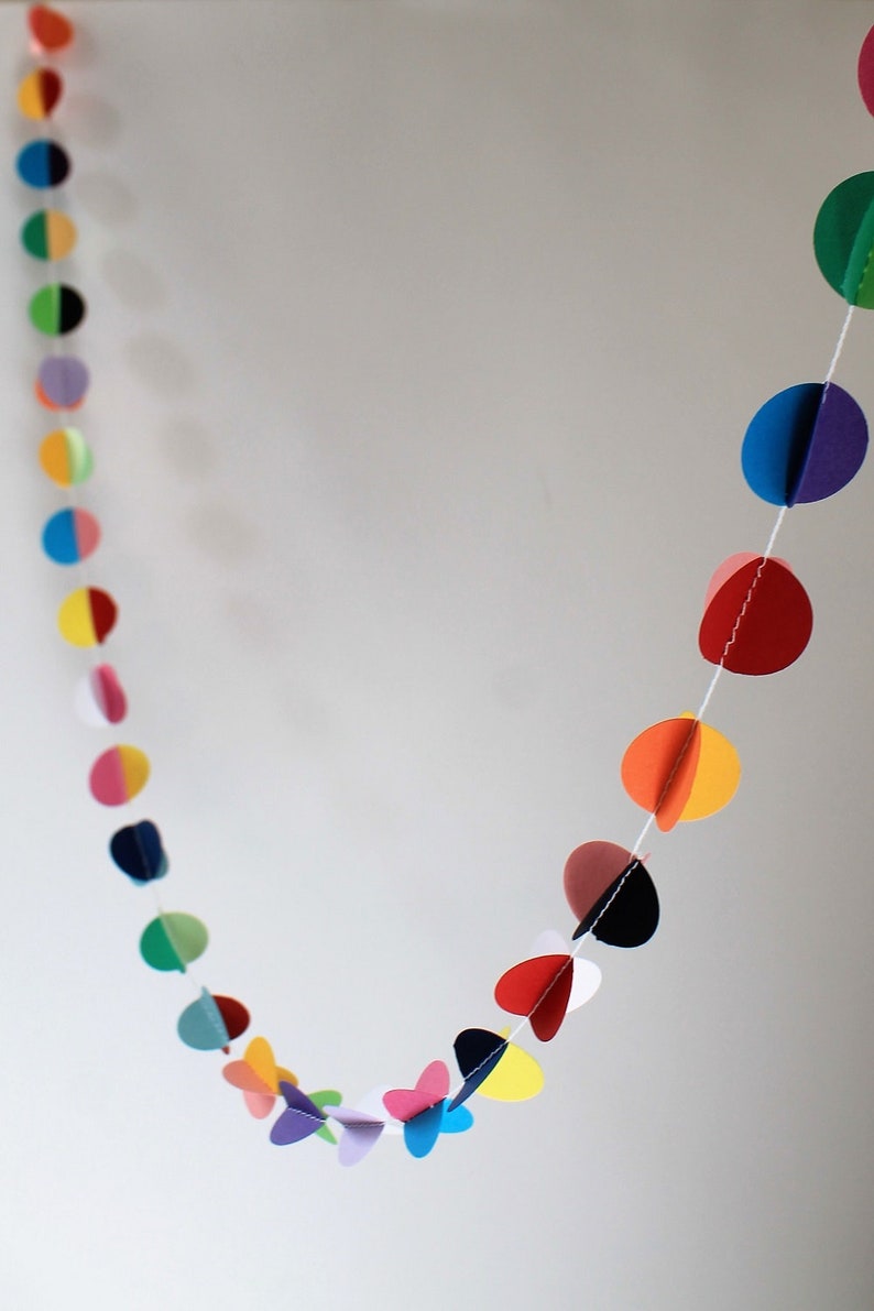 May include: A colorful paper garland with circles of different colors, including red, orange, yellow, green, blue, purple, and pink. The circles are connected by a white string.