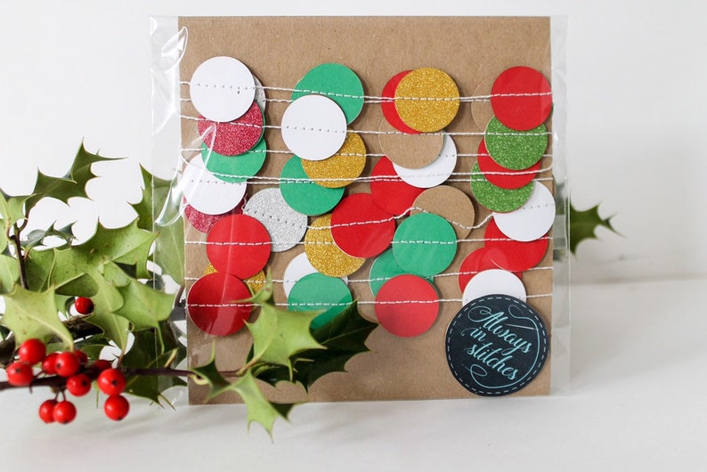 May include: A package of red, green, gold, white, and silver glitter paper circles strung together on white twine. The package is labeled "Always in Stitches".