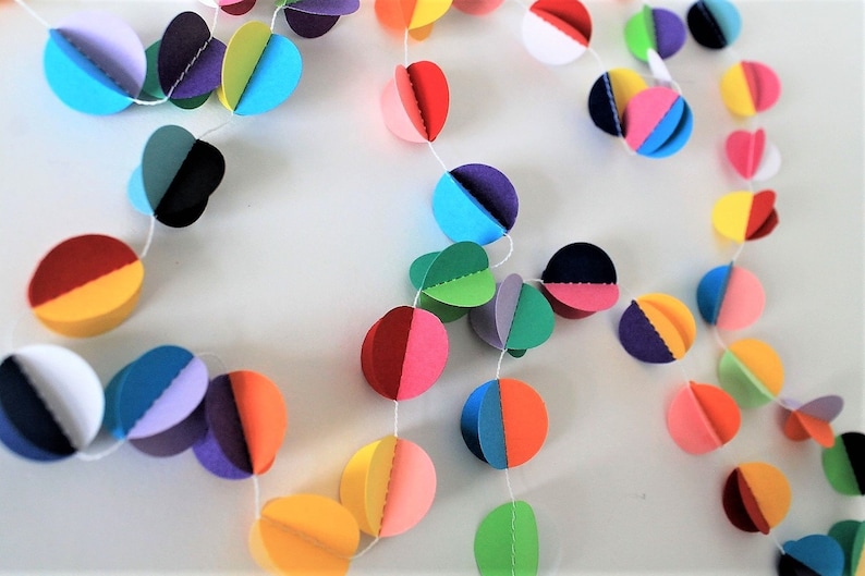 May include: A colorful paper garland with circles of different colors, including red, orange, yellow, green, blue, purple, and white. The circles are strung together with white thread.