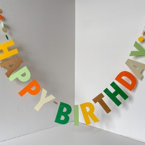 May include: A colorful paper banner with the words "Happy Birthday" in green, yellow, orange, and brown letters. The banner is strung with white thread and decorated with small circles in various colors.