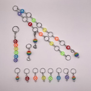 Peut inclure: Un ensemble de marqueurs de points de couleur arc-en-ciel avec des breloques en forme de cœur et les chiffres de 1 à 9. Les marqueurs sont attachés à une chaîne argentée avec des perles blanches.