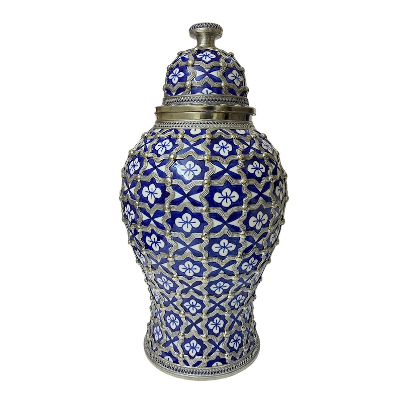 Puede incluir: Un jarr&oacute;n de cer&aacute;mica azul y blanco con tapa plateada y un intrincado patr&oacute;n floral. El jarr&oacute;n tiene un cuerpo redondo y un cuello estrecho.