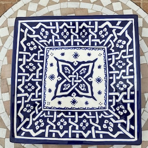 Peut inclure: Un plat de service carré en céramique avec un motif géométrique bleu et blanc. Le plat a une bordure surélevée et un motif central en forme d'étoile.