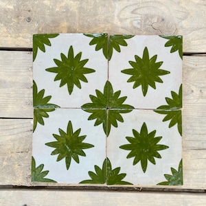 May include: Four square ceramic tiles with a white background and a green starburst design. The tiles are arranged together, showcasing the repeating pattern. The tiles are likely for use in a kitchen or bathroom.