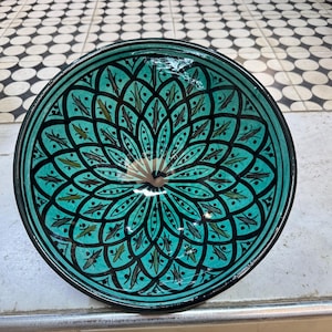 Peut inclure: Un bol en céramique turquoise avec un motif géométrique noir et vert. Le bol est de forme circulaire et a un bord large.