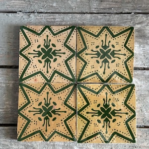 Puede incluir: Cuatro baldosas cuadradas con un diseño de estrella. Cada baldosa presenta un fondo beige con una estrella verde oscuro y un patrón floral. Las baldosas están dispuestas en forma cuadrada sobre una superficie de madera envejecida.