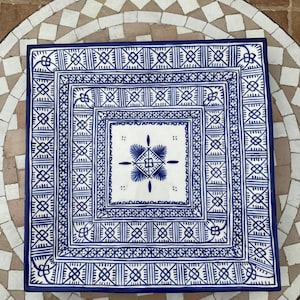 Peut inclure: Un plat de service carré en céramique avec un fond blanc et des motifs géométriques bleus complexes. Le design présente un motif central de fleur stylisée avec une forme de diamant.