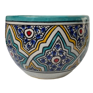 Op de afbeelding: Een witte keramische kom met een geometrisch patroon in blauw, geel en turquoise. De kom heeft een ronde vorm en een brede rand.