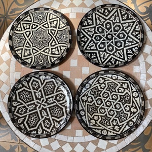 Może przedstawiać: Cztery czarne i białe ceramiczne talerze z misternymi geometrycznymi wzorami. Talerze mają podniesiony rant i błyszczące wykończenie.