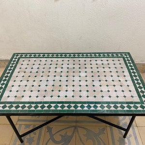 Könnte beinhalten: Ein quadratischer Couchtisch mit einer grünen und weißen gekachelten Tischplatte und einem schwarzen Metallgestell.