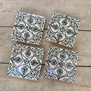 Puede incluir: Cuatro azulejos de cerámica blanca con intrincados patrones florales negros. Los azulejos son de forma cuadrada y tienen un acabado brillante.