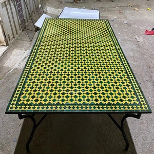 Może przedstawiać: Stół z czarnym metalowym stelażem i blatem z zielonych i żółtych płytek. Blat stołu ma wzór w romby.