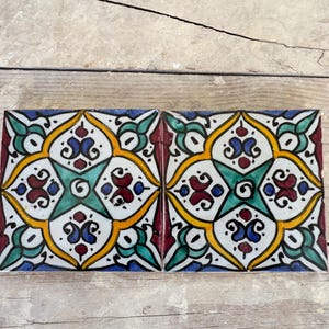 Puede incluir: Dos azulejos cuadrados de cerámica con un patrón geométrico colorido. El patrón presenta una forma de estrella en el centro con espirales y diseños florales en tonos de azul, verde, rojo, amarillo y blanco.