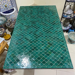 Könnte beinhalten: Eine grüne marokkanische Fliesentischplatte mit Fischschuppenmuster. Die Tischplatte besteht aus kleinen, grünen Fliesen, die in einem sich wiederholenden Muster angeordnet sind.