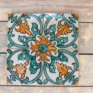 May include: Four square ceramic tiles with a floral pattern. The tiles are white with green and orange floral designs. The tiles are arranged in a square pattern.