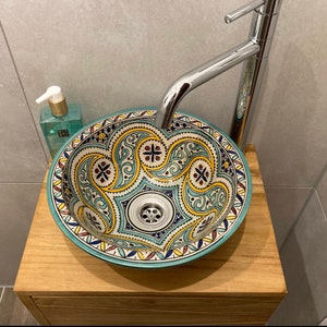 Puede incluir: Un lavabo de cer&aacute;mica turquesa y blanco con intrincados patrones florales amarillos y rojos. El lavabo est&aacute; montado en una encimera de madera con un grifo cromado.