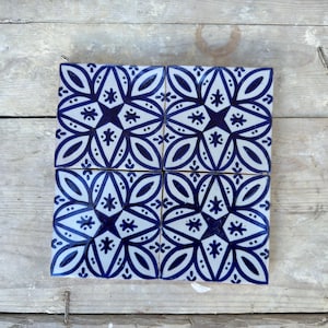 Könnte beinhalten: Vier quadratische Keramikfliesen mit einem blauen und weißen geometrischen Muster. Das Muster zeigt eine Sternform mit einer blauen Mitte und weißen Umrissen. Die Fliesen sind in einem 2x2-Raster angeordnet.
