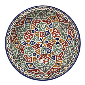 Puede incluir: Un tazón grande y redondo de cerámica con un borde azul y intrincados patrones geométricos en tonos de rojo, naranja, verde, azul y gris.