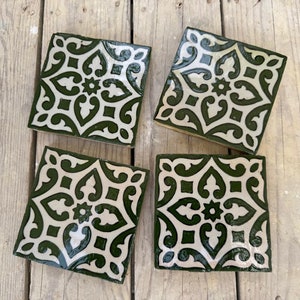 Op de afbeelding: Vier vierkante keramische tegels met een witte achtergrond en een groen geometrisch patroon. Het patroon heeft een centrale ster met vier gebogen bladeren die vanuit elk punt uitstrekken.