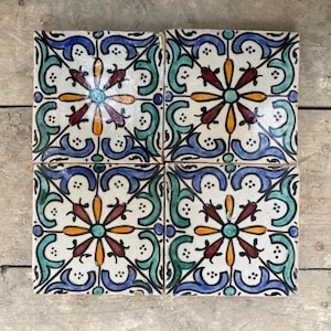 Puede incluir: Cuatro azulejos cuadrados de cerámica con fondo blanco y intrincados patrones florales azules, verdes, rojos y naranjas.