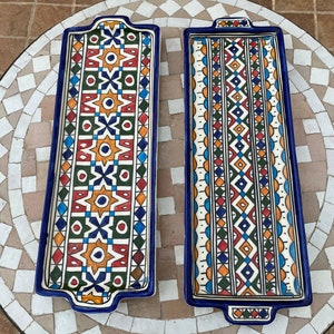 Könnte beinhalten: Zwei rechteckige Serviertabletts aus Keramik mit blauem Rand und komplizierten geometrischen Mustern in Rot-, Grün-, Gelb- und Blautönen.