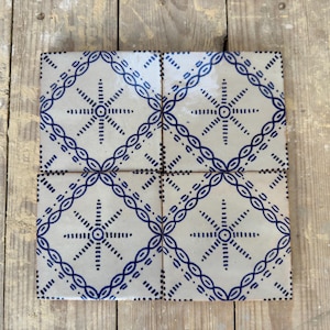 Op de afbeelding: Vier vierkante keramische tegels met een witte achtergrond en een blauw geometrisch patroon. Het patroon heeft een stervormig ontwerp in een ruitvorm.