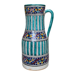 Peut inclure: Un pichet en céramique avec un motif rayé bleu et blanc et des motifs floraux complexes en rouge, jaune et bleu. Le pichet a une anse et une base arrondie.