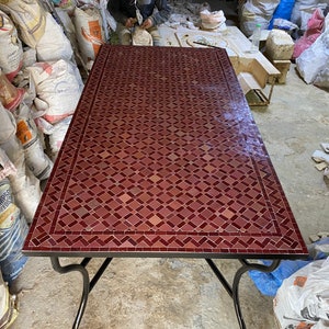 May include: A red Moroccan tile table with a diamond pattern. The table has a black metal frame with curved legs.