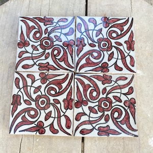 Op de afbeelding: Vier vierkante keramische tegels met een witte achtergrond en een herhalend patroon van zwarte en kastanjebruine bloemmotieven.